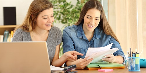 Peer Writing Tutors Two female students bent over laptop and text in exchange