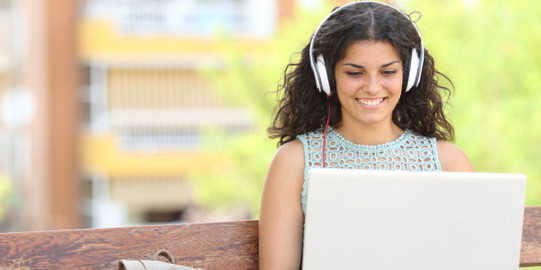 Studentin mit Kopfhörer und Laptop am Schoß