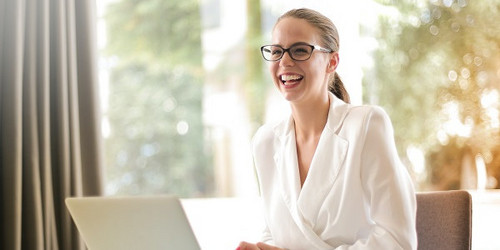 Female employee at desk in front of laptop, looks up and smiles warmly