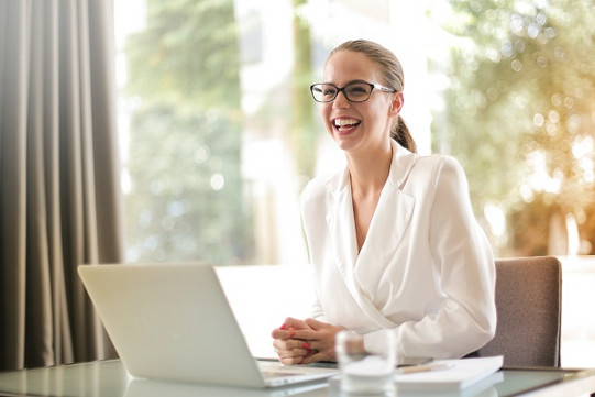 Female employee at desk in front of laptop, looks up and smiles warmly