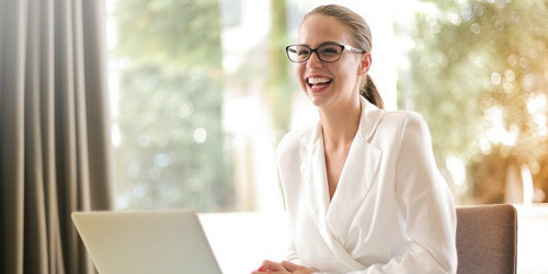 Female employee at desk in front of laptop, looks up and smiles warmly