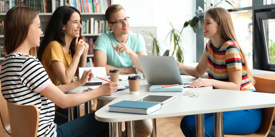 Schreibgruppe 4 Studierende in Lernsituation, im Halbkreis um einen Tisch sitzend, im Gespräch