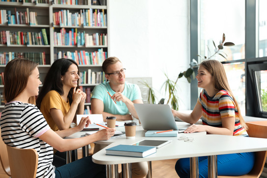 4 students in a study situation, sitting in a semicircle around a table, in conversation