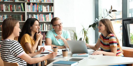 4 students in a study situation, sitting in a semicircle around a table, in conversation