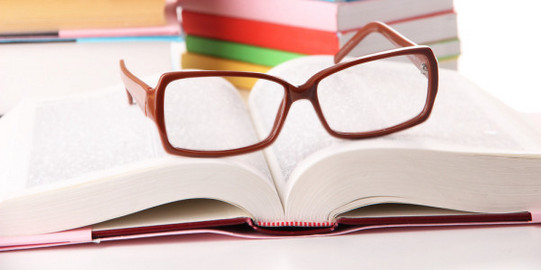 Stack of books in background, opened book and reading glasses in foreground