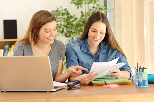 Zwei weibliche Studierende über Laptop und Text gebeugt im Austausch